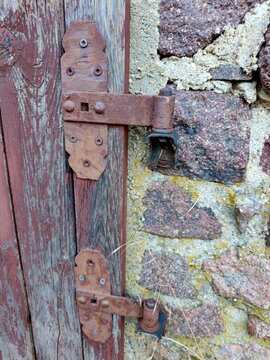 An old, rusty metal hinge on the wooden door of a stone building.