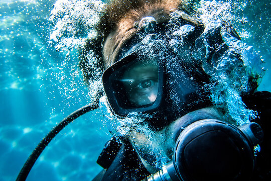Scuba diver face wearing diving mask with oxygen bubbles underwater