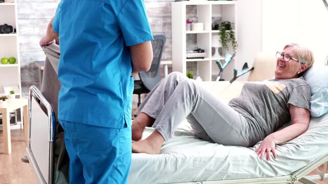 Nurse helps a senior woman settle into bed and covers her with a blanket, providing comfort, practical assistance and attentive residential care.