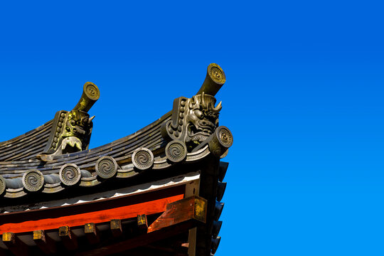 A traditional Japanese roof corner adorned with onigawara against a blue sky. The demon-faced roof tile is traditionally used in Japanese architecture to protect buildings and scare away evil spirits.