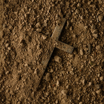 Christian cross buried in dirt being uncovered. Crucifix in dirt symbolic of death, loss, or burial. Finding a Christian cross symbolizing rediscovering of faith or the resurrection of Jesus Christ.
