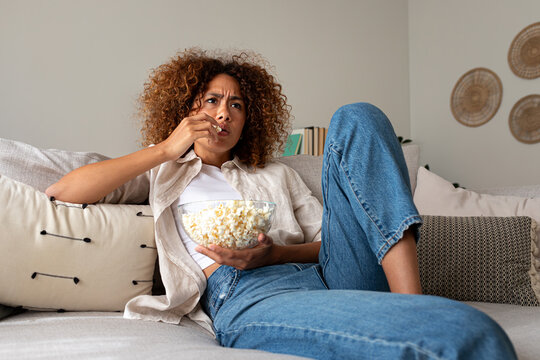 Woman focusing while eating popcorn and relaxing on sofa