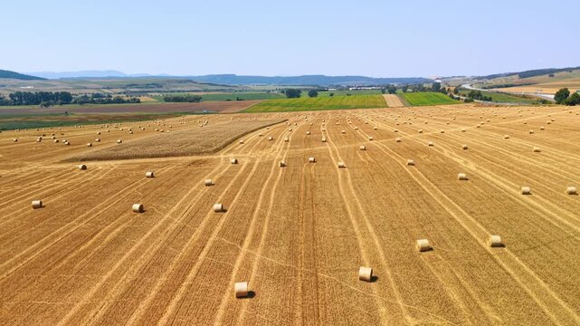 Straw bales across a harvested field in Slovakia. An elevated view shows cylindrical bales among parallel crop rows, with a highway in the distance.
