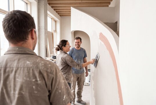 Group of professional builders and plasterers smiling while applying plaster on a curved wall during interior home renovation
