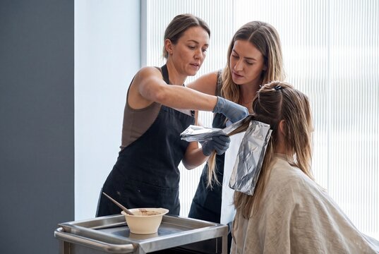 Professional female hair stylists applying highlights and color treatment to a client using foil in a modern beauty salon