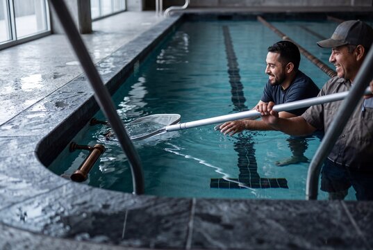 Two pool service technicians working together to clean an indoor lap pool using a skimmer net