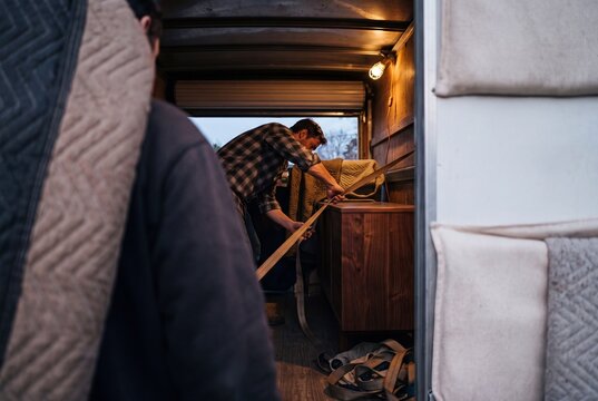 Man securing wooden furniture with tie-down straps inside a cargo moving truck during home relocation