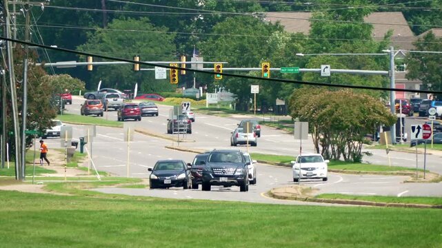 Cars, trucks and vehicles move quickly in both directions on a busy road street used for commuting and commerce with stoplights and street signs on a bright sunny day.
