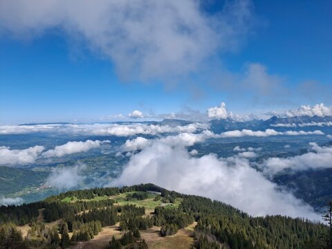 un magnifique paysage de montagne, o&ugrave; une impressionnante mer de nuages blancs flotte au-dessus d'une vall&eacute;e verdoyante, sous un ciel bleu intense