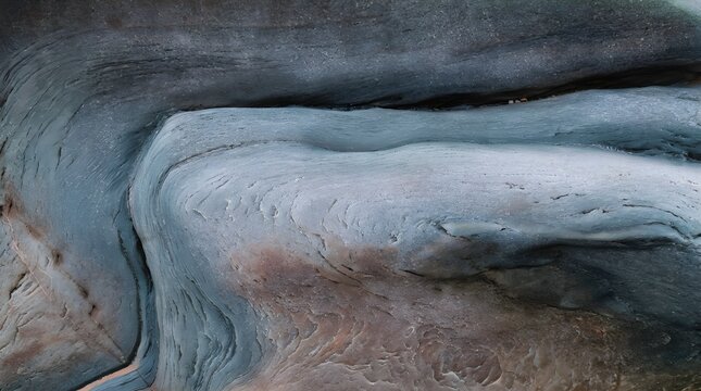 An extraordinary, dramatic aerial view of flowing silver-blue water streams cutting soft winding curves through pale sand sediments.