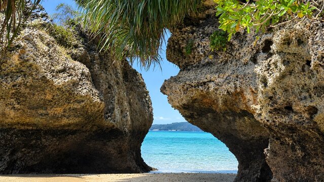 A dramatic and alluring natural landscape looking out between towering coastal limestone cliffs into a sheltered turquoise sea cove under blue skies