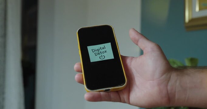 Person places a &ldquo;Digital Detox&rdquo; sticky note on smartphone, concept of reducing screen time, disconnecting from technology and taking a break from social media.