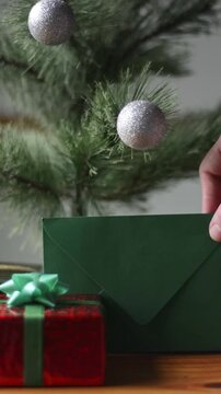 Close up of male hand leaving green envelope near gift boxes under Christmas tree