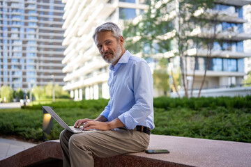 Fototapeta premium Mature businessman working remotely using laptop outdoors