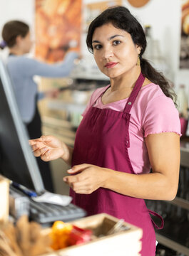 Attentive young waitress in apron checking orders on monitor in modern cafeteria