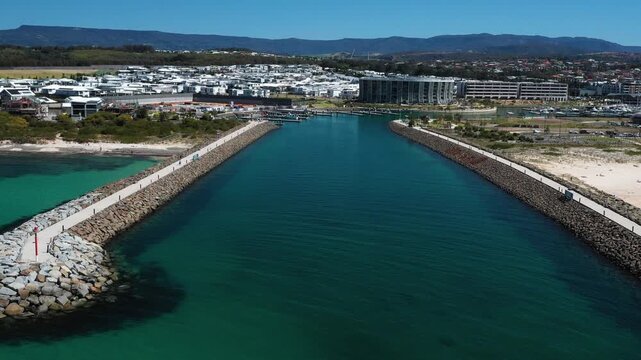 Aerial panning view of the Shell Cove breakwater and turquoise blue ocean entrance leading to the scenic Shellharbour Marina, situated on the Illawarra South Coast of New South Wales, Australia. 