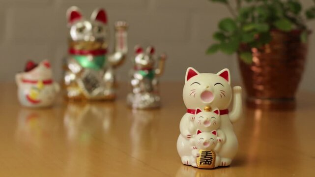 Video de gato de la suerte Maneki Neko moviendo la pata en su vientre tiene 3 gatitos, al fondo desenfocado m&aacute;s gatos
