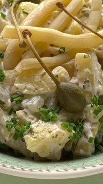 Potato salad with a twist: swap out pickled cucumbers for fermented yellow snap beans and garnish with caper berries. Presented on a pastel green background, with a rotating table and vertical video.