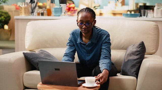 Portrait of female digital nomad using laptop at kitchen table, enjoying relaxed freelancer lifestyle with flexible work, adult woman telecommuting indoors.