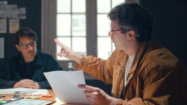 Emotional male filmmaker explaining script points to his colleagues during preproduction meeting or brainstorming session in creative studio