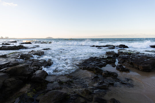 Waves crashing against dark, weathered rocks in a rocky coastal shoreline