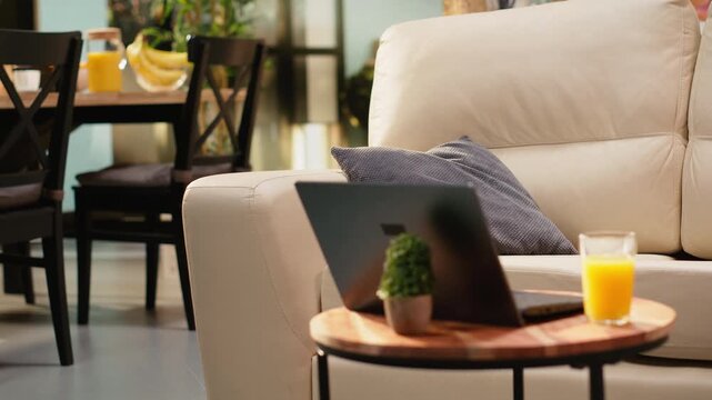 Empty coffee table with orange juice glass sits in a living room with rustic natural light, cozy interior and wooden furniture. Open floor plan has no people and morning light fills the room.