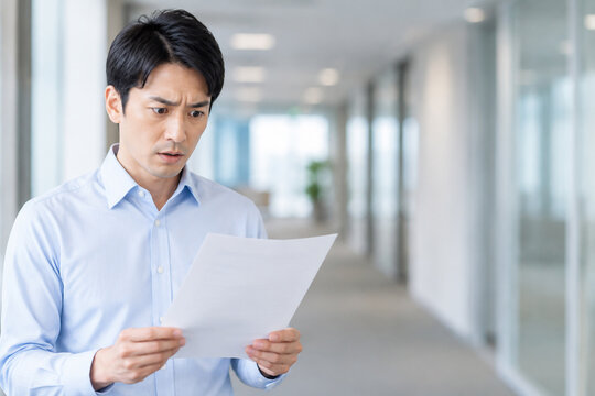 オフィスの廊下で書類を見て驚く男性ビジネスマン