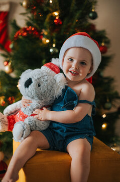 Blonde child hugs a koala teddy bear with a big smile by a Christmas tree