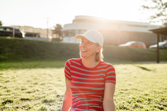 Woman in stripe shirt, sitting in a grassy park under the warm afternoon sun, smiling and relaxed.