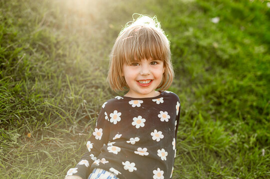 A joyful young child with a cheerful smile sitting on green grass enjoying a warm sunny day
