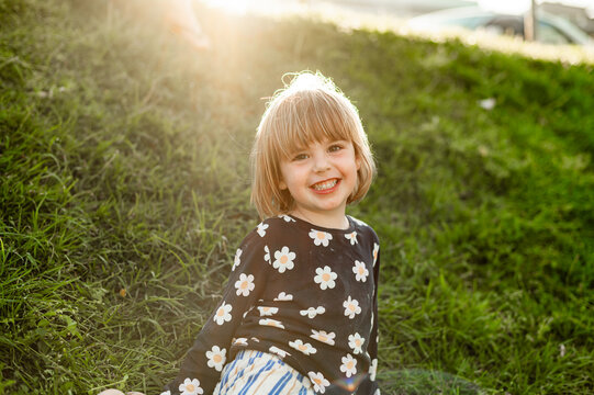 Smiling child sitting on green grass, in the warm sunlight during the afternoon