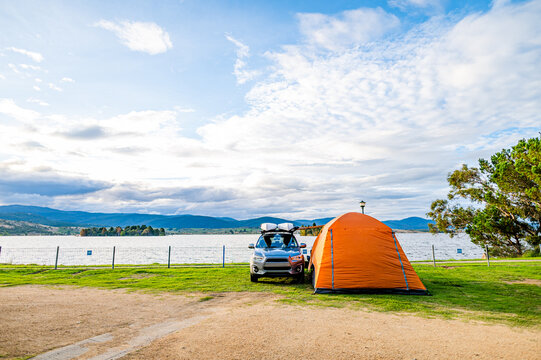 Orange tent and silver SUV parked beside scenic lakeside