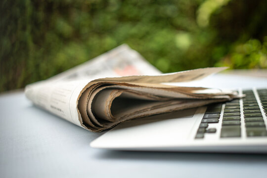Newspaper on top of computer laptop outdoor.