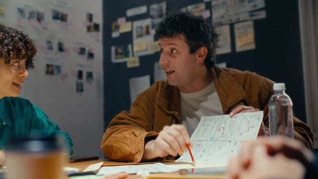 Man presenting scenes on storyboard sketch and brainstorming with team during film preproduction meeting in office