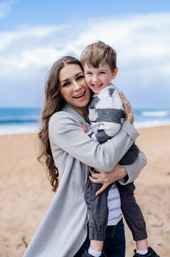 Joyful moment of a mother holding her son at the beach with ocean waves in the background