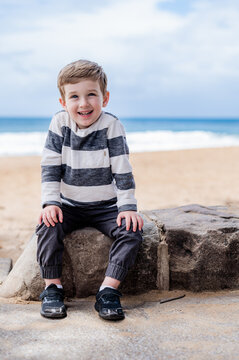 Young boy smiles while sitting on a rock near the beach with ocean in the background