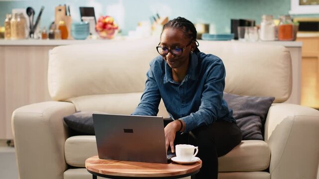 Adult woman working from home in cozy rustic living room, using laptop for daily tasks online. Freelancer lifestyle with remote work setup and natural light supporting productivity at home.