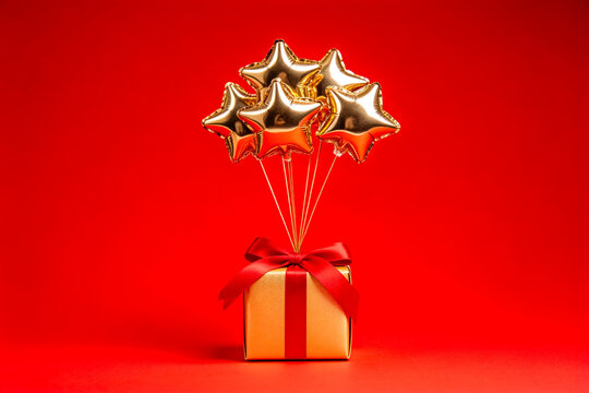 Golden Star Balloons Attached to Gift Box on Red Background