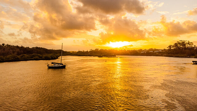 sailing boat at vibrant sunset reflections on wide river estuary