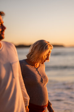 Couple walking hand in hand at Manly Beach during sunrise, celebrating maternity and family