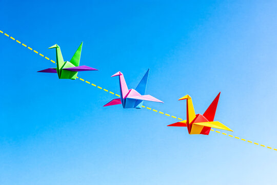 Three Colorful Origami Cranes Flying Against Clear Blue Sky