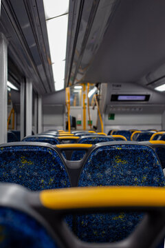 Empty passenger train carriage showing rows of blue patterned seats with yellow handles
