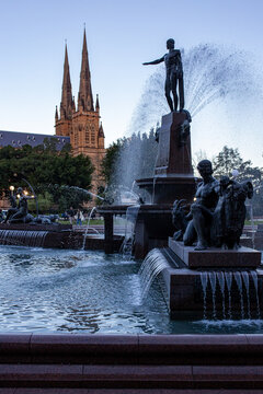 Ornate bronze fountain spraying water near twin spires of historic cathedral in city park