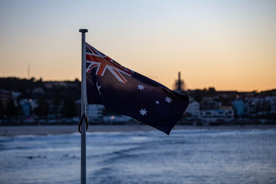 Australian flag fluttering gently on a flagpole near the coast during sunset