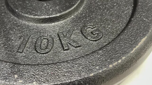 Close-up view of a dark grey heavy iron barbell weight plate with 10KG embossing text. Gym equipment, fitness training, bodybuilding workout.