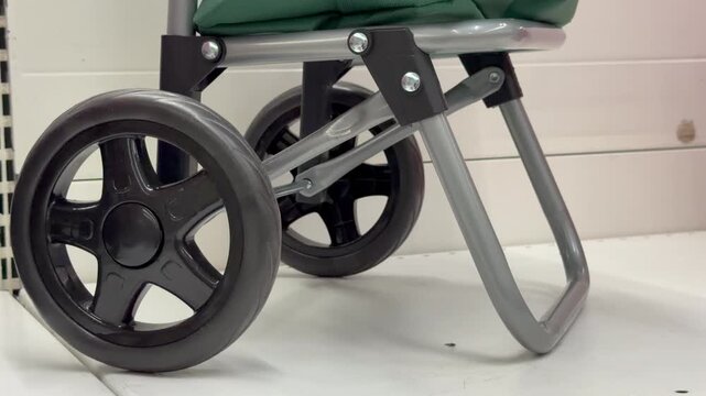 Close-up view of a black plastic wheel on a metal folding shopping trolley cart indoors. Utility equipment, household storage accessory, domestic transportation tool.