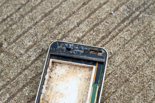 a badly damaged, dirty, and screenless smartphone frame lying on a concrete road surface