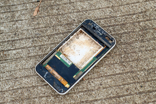 a badly damaged, dirty, and screenless smartphone frame lying on a concrete road surface
