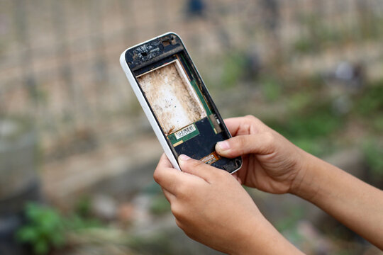 Close up of a person's hand holding a badly damaged, dirty, and screenless smartphone frame.