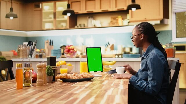 Vertical mockup green screen on tablet in kitchen at wooden table, with chroma key editable blank screen for teleworking indoors, remote work and productivity at home in interior with wireless tasks.
